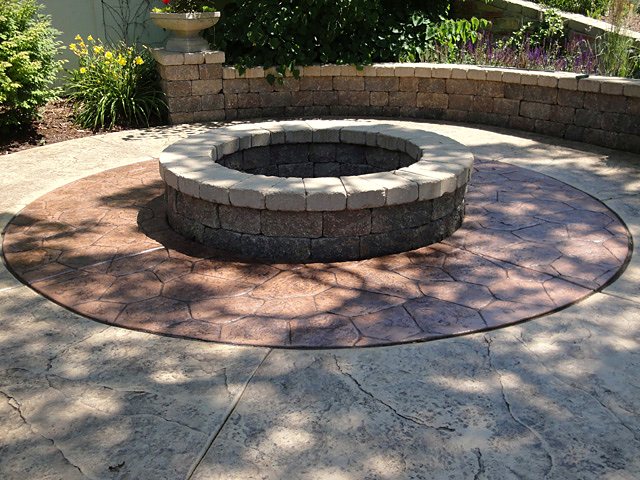 Circular stamped concrete patio with a stone fire pit and seat wall
